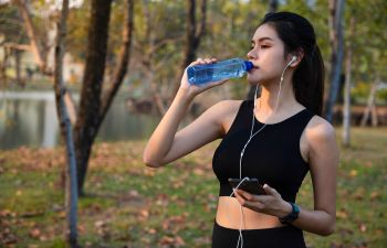 Athletic young woman drinking water after jogging in a park.