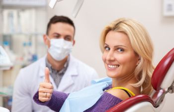 Satisfied smiling woman in a a dental chair showing her thumb up.