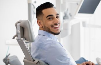 A happy young man with a perfect smile sitting in a dental chair after treatment.