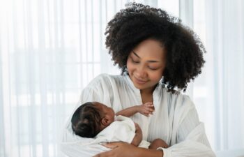 Close up portrait of beautiful young African American mother holding sleep newborn baby in hospital bed room. Healthcare medical love black afro woman lifestyle mother's day, breast with copy space.